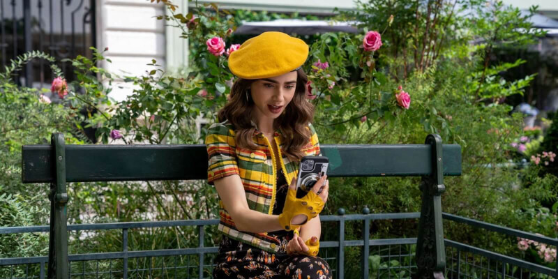 Hlavní postava Emily sedící v pařížském parku na lavičce.